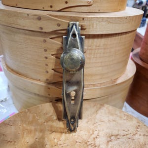 Könnte beinhalten: Ein antiker Messing-Türknopf mit einem Schlüsselloch und einem Art-Deco-Design.