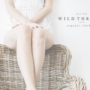 May include: A woman sits on a wicker chair with her legs crossed. The background is white with the text "WILD THREADS organic clothing" and "Estd. 2020".