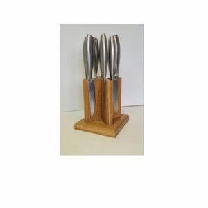 May include: A wooden knife block with five silver knives inserted into it. The block is made of light brown wood and has a square base.
