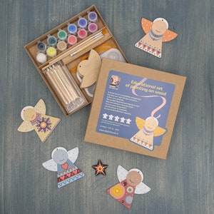 Può includere: Un kit creativo per dipingere ornamenti di angeli in legno. Il kit include colori, pennelli e angeli in legno con motivi colorati. La scatola presenta il testo "Educational set of painting on wood".