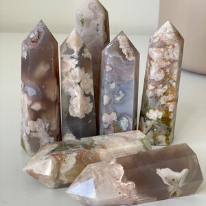 May include: A collection of six grey, white, and pink agate crystal points. The points are all different sizes and shapes, and they have a variety of patterns and textures.