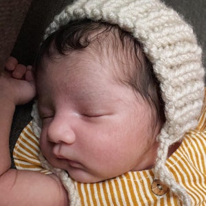 May include: A sleeping baby wearing a white crocheted bonnet and a yellow and white striped onesie.