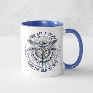 Pode incluir: Caneca de cerâmica branca com borda e alça azuis. A caneca apresenta um desenho de libélula azul e branca com o texto "Sing me a song of a lass that is gone, cold that lags, merry of soul, she sped on a tide over the sea to strive."