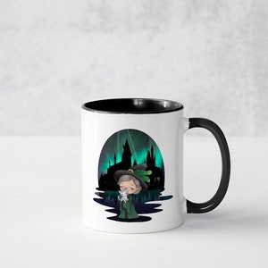 May include: White ceramic mug with a black rim and handle. The mug features a cartoon illustration of a woman in a witch's hat and robe, holding a white cat. The background is a silhouette of a castle with a green and blue aurora borealis.