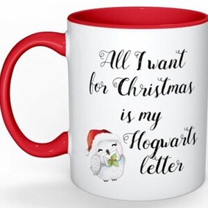 Puede incluir: Taza de cer&aacute;mica blanca con borde y asa rojos. La taza tiene un b&uacute;ho blanco con un gorro de Pap&aacute; Noel y sosteniendo una carta. El texto en la taza dice "All I want for Christmas is my Hogwarts letter."