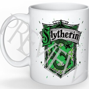Op de afbeelding: Witte keramische mok met een groen en zwart Slytherin-huiswapen uit de Harry Potter-serie. Het wapen toont een slang en de woorden "Slytherin" op een banner.