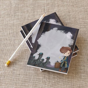 May include: A stack of blank notepads with a whimsical illustration of a boy with a wand and a group of creatures with glowing eyes. The illustration is set against a dark forest background with a full moon.