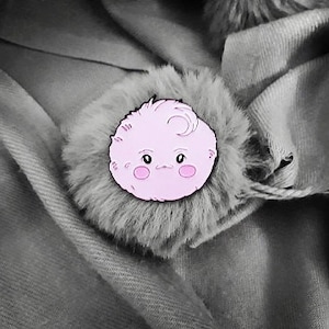 Może przedstawiać: Różowa, puszysta postać z jednym okiem i zarumienionymi policzkami. Postać jest przypinką na szarym, puszystym tle.