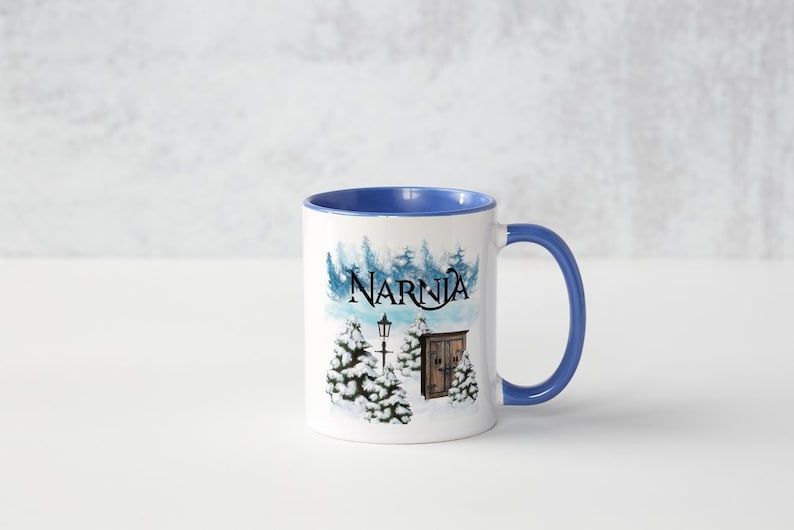 May include: A white ceramic mug with a blue rim and handle. The mug features a winter scene with a lamppost, a wooden door, and trees covered in snow. The text "Narnia" is printed in black on the mug.