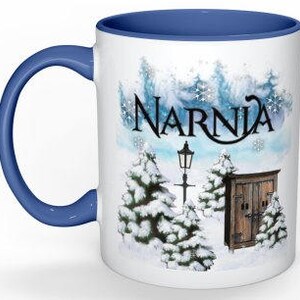 May include: White ceramic mug with a blue rim and handle. The mug features a winter scene with snow-covered trees, a lamppost, and a wooden door with the word "Narnia" written in a stylized font.