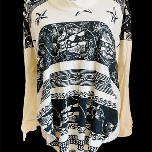 May include: A cream-colored long-sleeved shirt with a black and white print of nautical themed designs. The shirt has a high neck and a loose fit.
