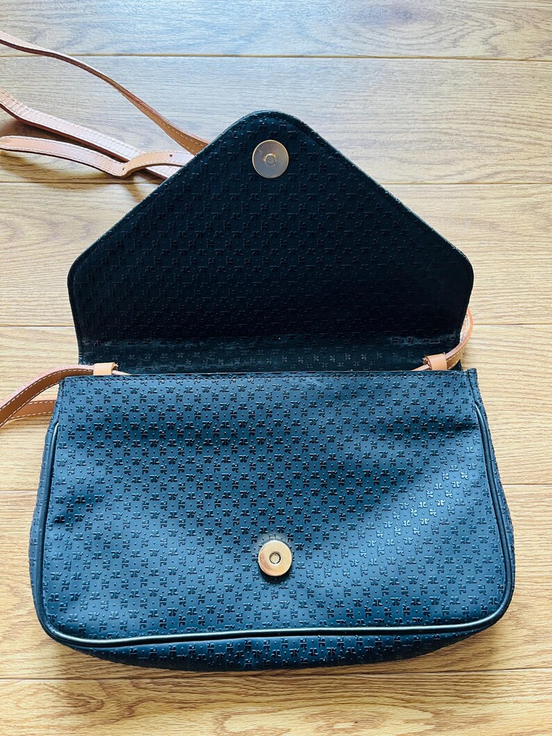May include: A black crossbody bag with a geometric pattern and a tan strap. The bag has a flap closure with a gold-colored magnetic snap. The interior is black, and the bag appears to be made of a textured fabric.