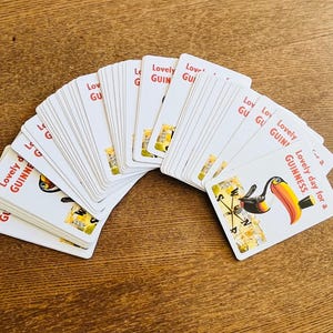 May include: A deck of white playing cards with the text "Lovely Guinness" and a toucan illustration. The cards are fanned out on a wooden surface, showcasing the design.