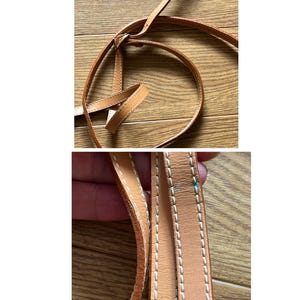 May include: Close-up of a light brown leather strap with white stitching. The strap is looped and knotted, suggesting it is part of a bag or accessory. The leather appears to be well-worn.