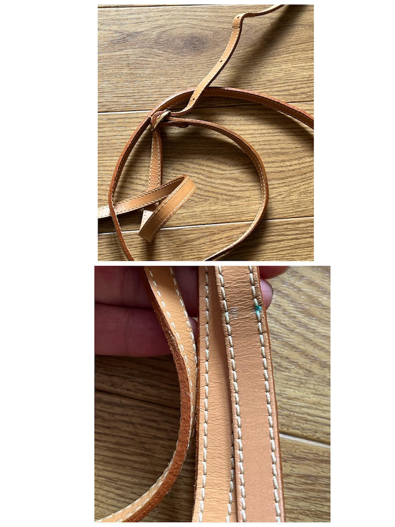 May include: Close-up of a light brown leather strap with white stitching. The strap is looped and knotted, suggesting it is part of a bag or accessory. The leather appears to be well-worn.