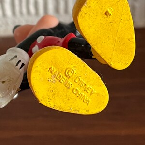 May include: Yellow plastic Mickey Mouse figurine with a red shirt and black shorts. The bottom of the figurine has the text "&copy; Disney Made in China".