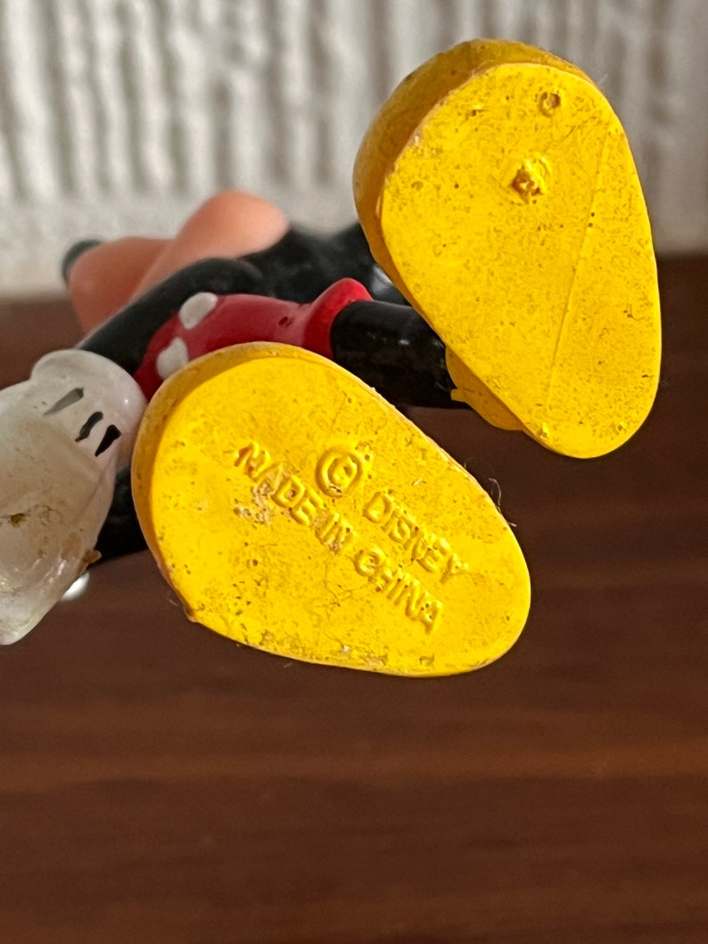 May include: Yellow plastic Mickey Mouse figurine with a red shirt and black shorts. The bottom of the figurine has the text "&copy; Disney Made in China".