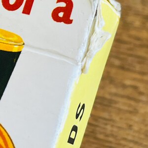 May include: Close-up of a card game box with the words "for a" in red letters on a white background. The side of the box is yellow with the word "CARDS" in black letters. The box is on a wooden surface.