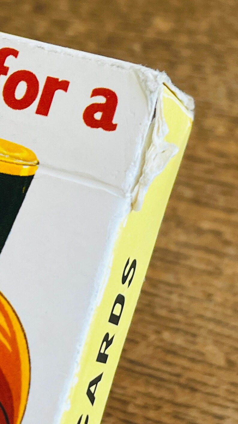 May include: Close-up of a card game box with the words "for a" in red letters on a white background. The side of the box is yellow with the word "CARDS" in black letters. The box is on a wooden surface.
