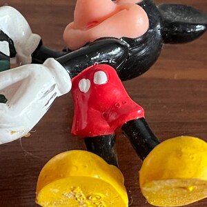 May include: A black and red plastic Mickey Mouse figurine with yellow shoes. The shoes have the copyright symbol and the year 1988 printed on the bottom.
