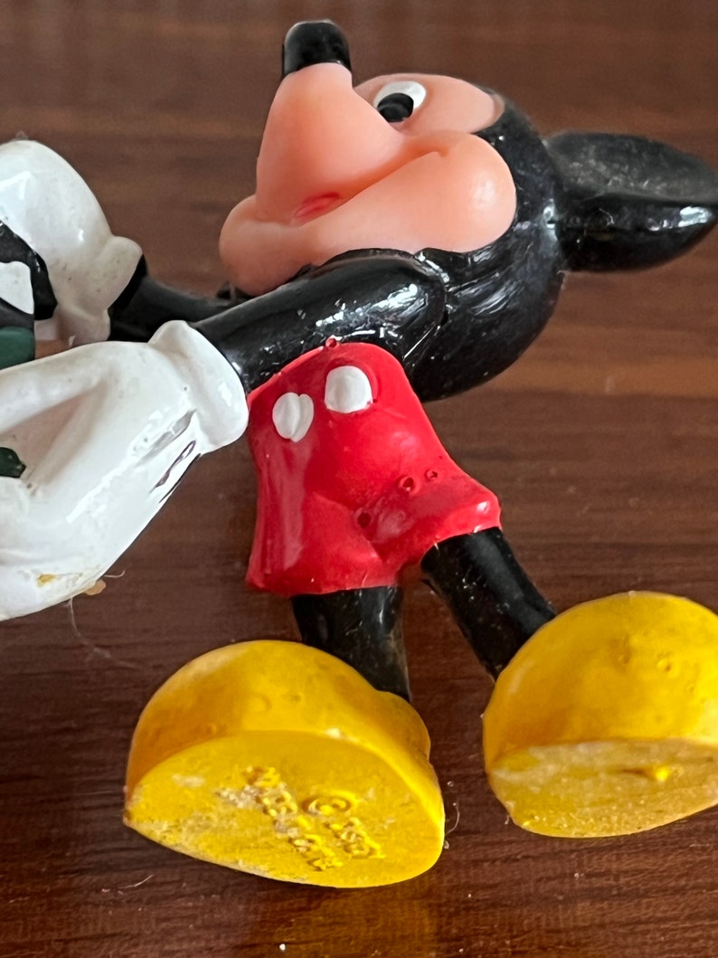 May include: A black and red plastic Mickey Mouse figurine with yellow shoes. The shoes have the copyright symbol and the year 1988 printed on the bottom.