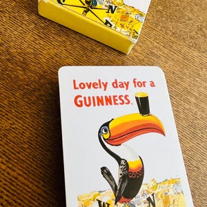 May include: Two Guinness playing cards with a toucan illustration. The cards feature the text "Lovely day for a Guinness" in red. The toucan has a large orange and yellow beak and is holding a pint of Guinness.