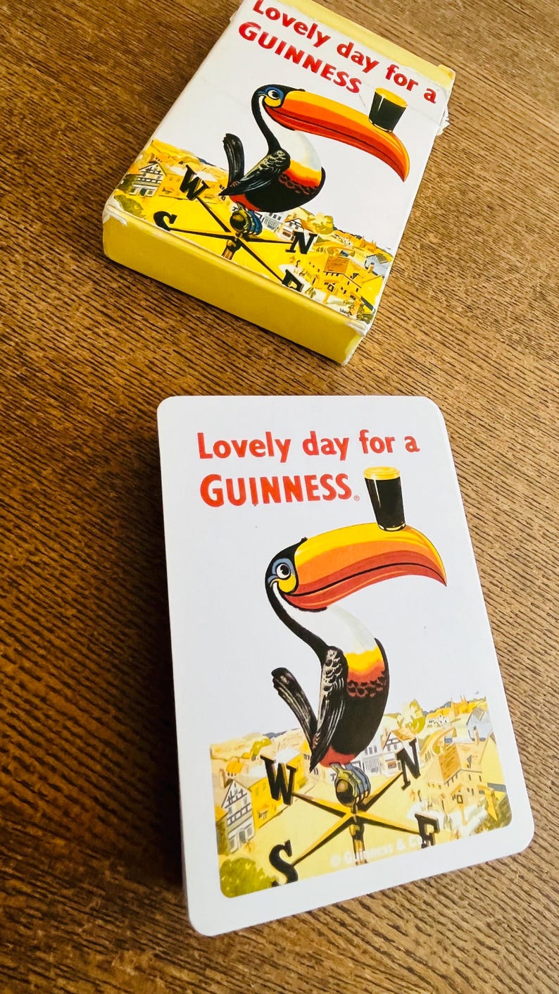 May include: Two Guinness playing cards with a toucan illustration. The cards feature the text "Lovely day for a Guinness" in red. The toucan has a large orange and yellow beak and is holding a pint of Guinness.