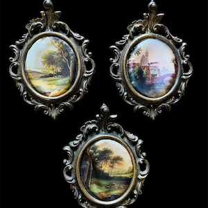 May include: Three antique oval framed landscape paintings. Each painting depicts a different rural scene with trees, fields, and buildings. The frames are ornate, with a bronze finish, and are set against a black background.