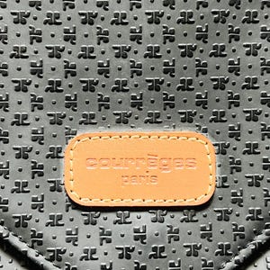 May include: Black leather handbag with a repeating embossed pattern. A rectangular tan leather patch with the words "courr&egrave;ges paris" is centered on the front of the bag. The bag has a flap closure.