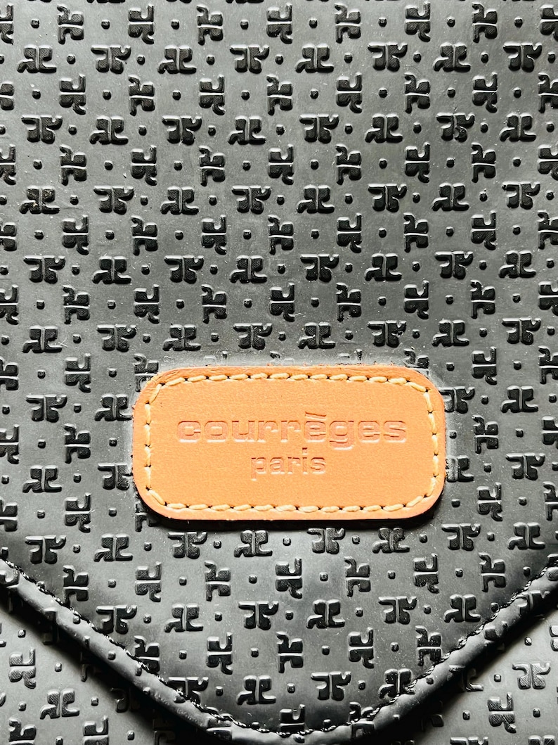 May include: Black leather handbag with a repeating embossed pattern. A rectangular tan leather patch with the words "courr&egrave;ges paris" is centered on the front of the bag. The bag has a flap closure.