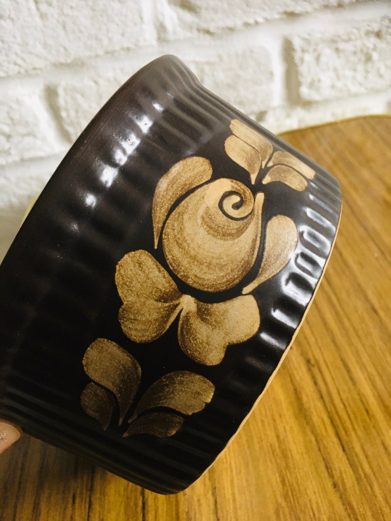 May include: A brown ceramic baking dish with a decorative floral design in a lighter brown color. The dish has a fluted rim.