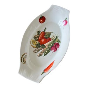 May include: White oval serving dish with a colorful vegetable design. The illustration includes a tomato, carrots, peas, radishes, and asparagus. The dish has a slightly textured rim and is ideal for serving salads or side dishes.