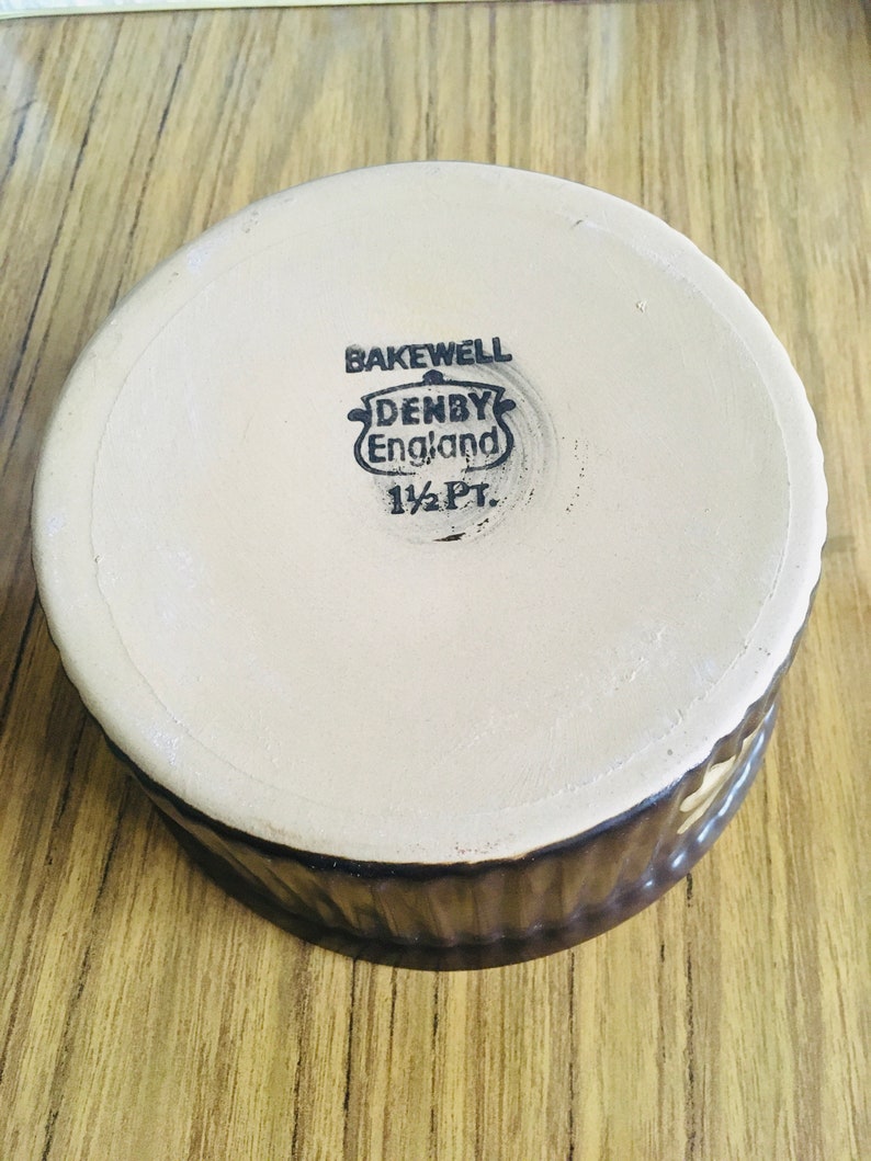 May include: A brown ceramic baking dish with a white interior. The bottom of the dish has a black stamp that reads "Bakewell Denby England 1 1/2 Pt."