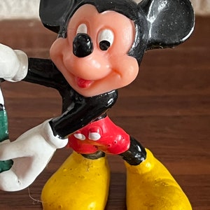May include: A black and red plastic figurine of Mickey Mouse. Mickey is wearing yellow shoes and has a big smile.