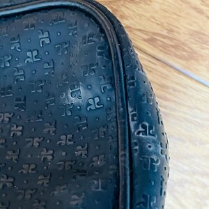May include: Close-up of a black, textured bag with a repeating pattern of stylized letter "R" shapes. The bag has a rounded shape and a black trim. The surface shows signs of wear.