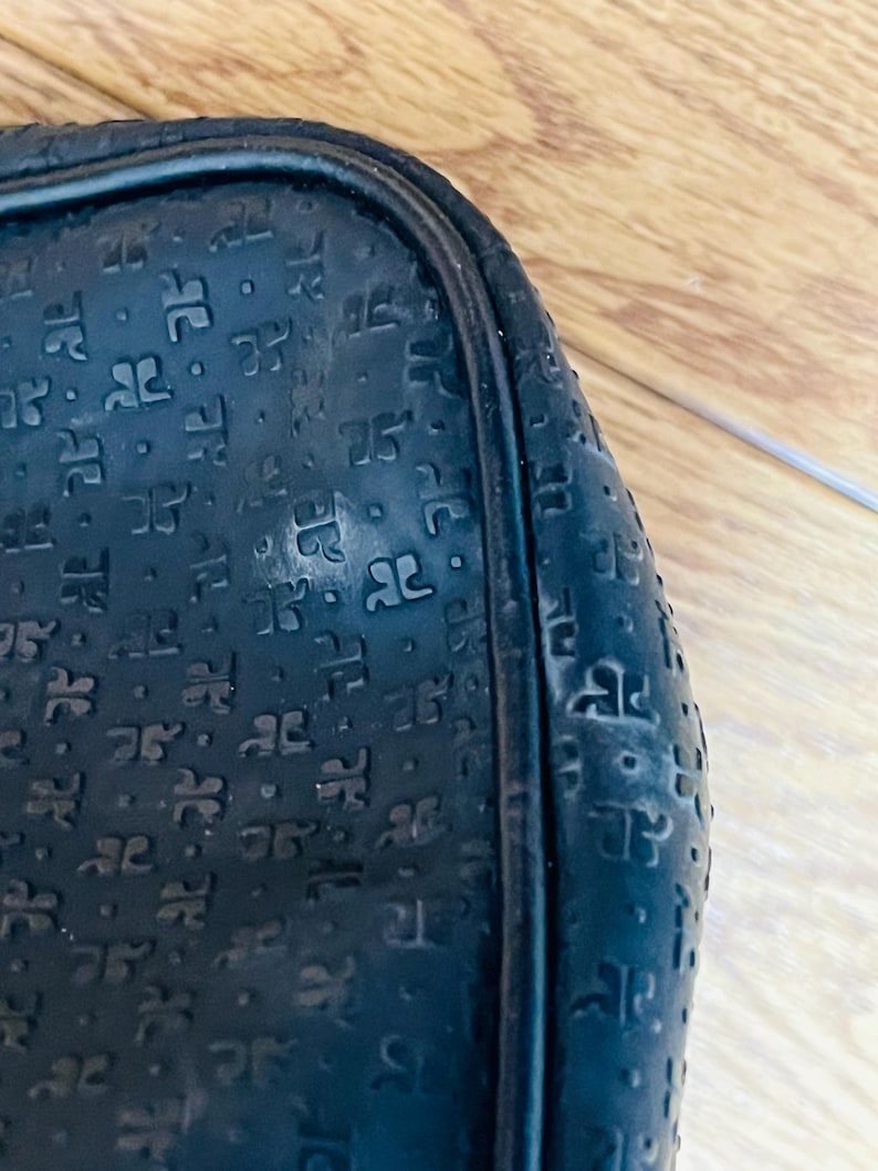 May include: Close-up of a black, textured bag with a repeating pattern of stylized letter "R" shapes. The bag has a rounded shape and a black trim. The surface shows signs of wear.