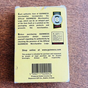 May include: A rectangular GUINNESS merchandise box with text and a logo. The box is yellow and black, with the GUINNESS logo in the upper right corner. The text describes the authenticity of the merchandise.