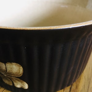 May include: A brown ceramic baking dish with a white floral design. The dish has a fluted edge and is made of stoneware.