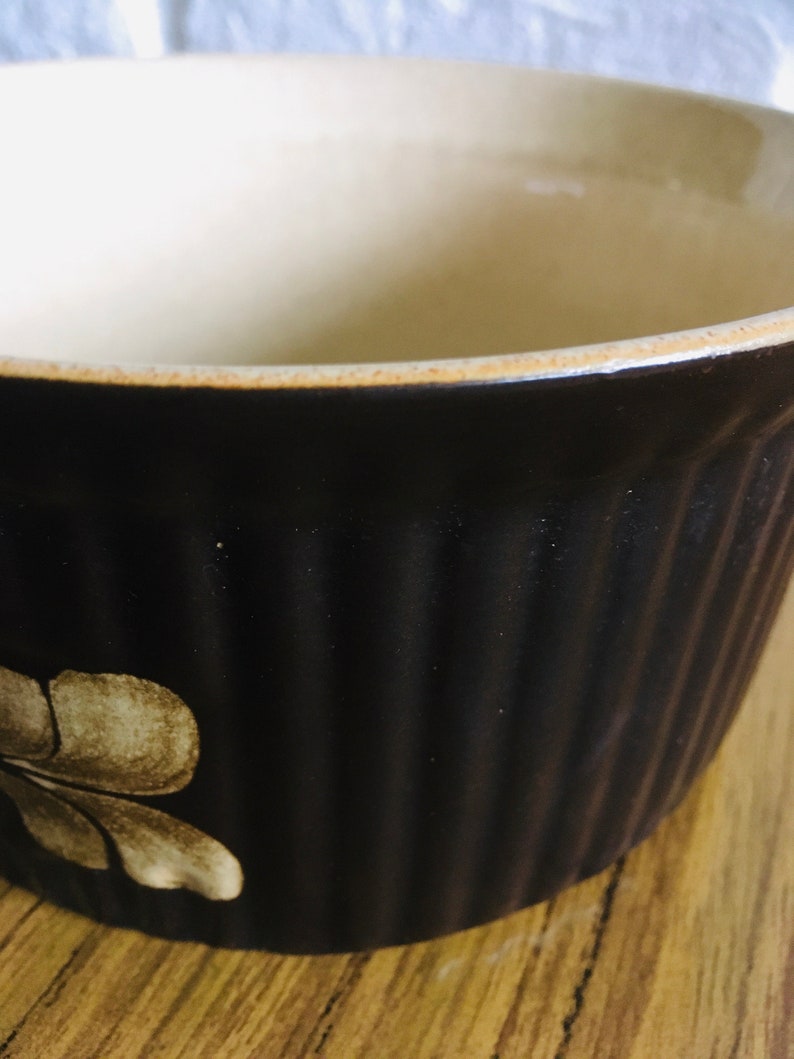 May include: A brown ceramic baking dish with a white floral design. The dish has a fluted edge and is made of stoneware.