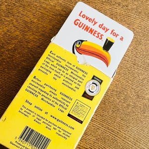 May include: A yellow and white GUINNESS merchandise box with the text "Lovely day for a GUINNESS". The box features a toucan illustration and product information. The box is intended for alcohol beverage enjoyment.