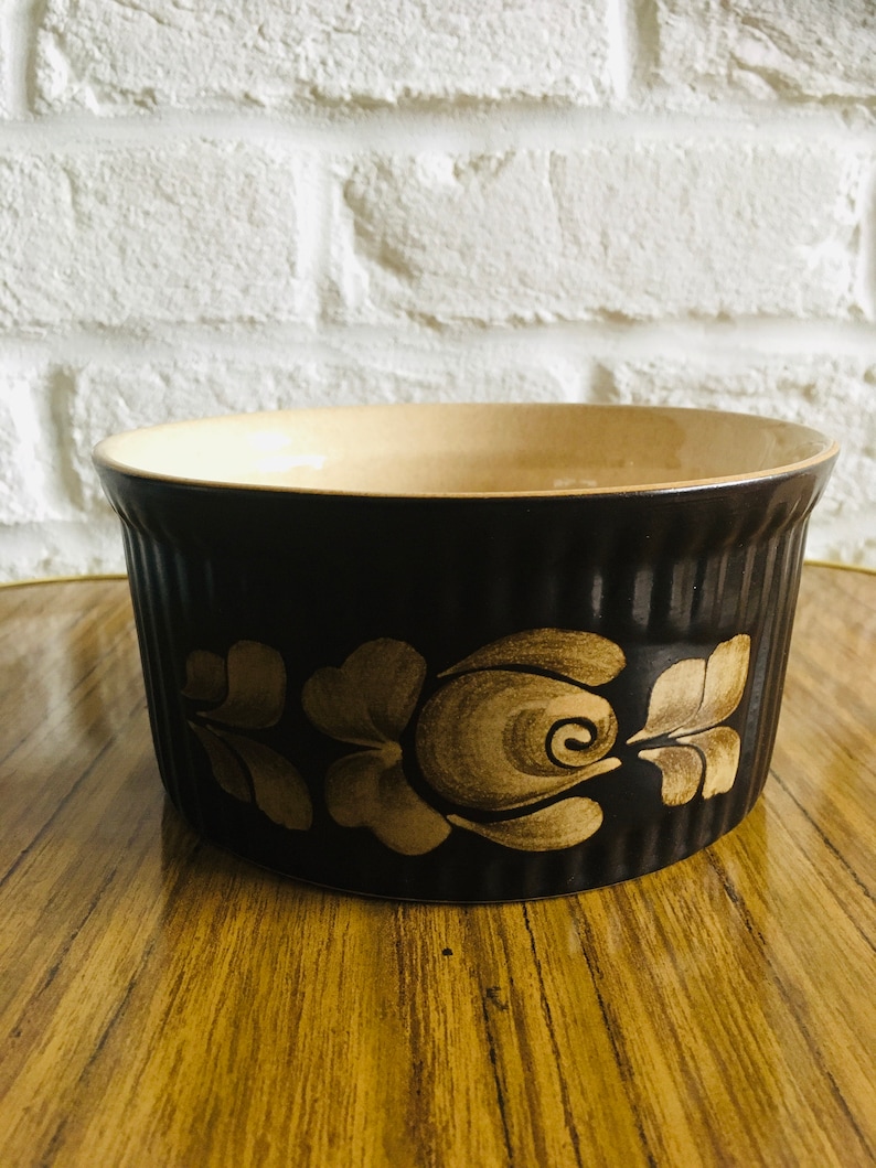 May include: A brown ceramic baking dish with a floral design in a lighter brown color. The dish has a fluted rim and is perfect for baking casseroles, desserts, or other dishes.