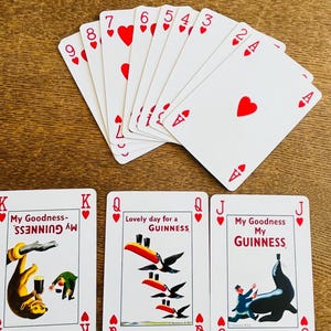 May include: A collection of playing cards featuring a Joker card, a fan of red cards, and three Guinness-themed cards. The red cards display hearts and numbers. The Guinness cards have illustrations of a monkey, toucans, and a seal.