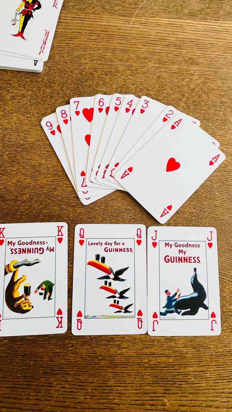May include: A collection of playing cards featuring a Joker card, a fan of red cards, and three Guinness-themed cards. The red cards display hearts and numbers. The Guinness cards have illustrations of a monkey, toucans, and a seal.