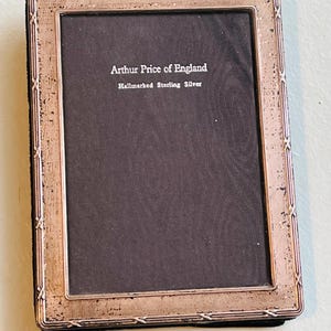 May include: An antique silver photo frame with a dark gray interior. The frame is rectangular with a decorative border. The text "Arthur Price of England Hallmarked Sterling Silver" is visible.