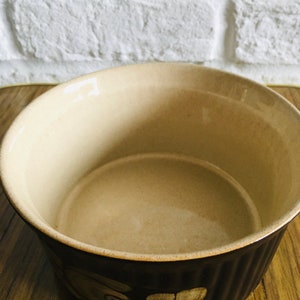 May include: A brown ceramic baking dish with a floral design. The dish has a white interior and a brown exterior with a raised rim.