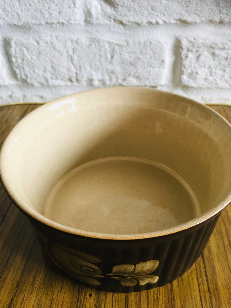 May include: A brown ceramic baking dish with a floral design. The dish has a white interior and a brown exterior with a raised rim.