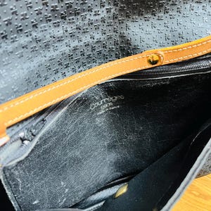 May include: Black leather handbag with a textured pattern and a tan leather strap. The interior is visible, showing the brand name "Courr&egrave;ges Paris made in france". The bag has a gold-colored clasp.