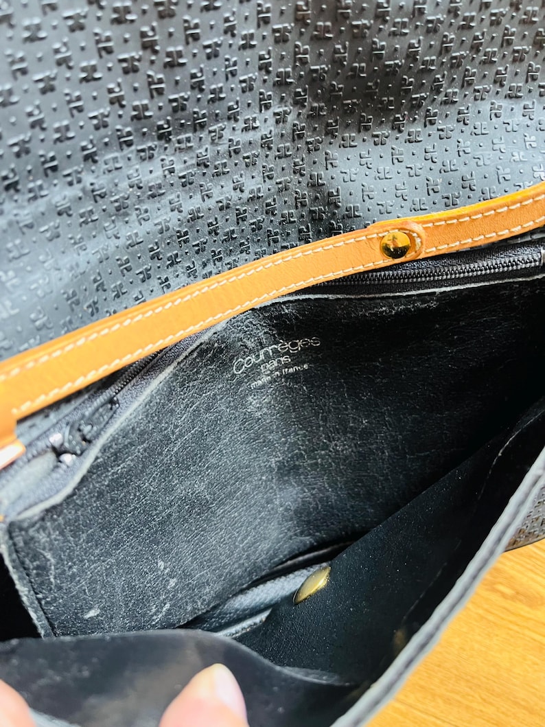 May include: Black leather handbag with a textured pattern and a tan leather strap. The interior is visible, showing the brand name "Courr&egrave;ges Paris made in france". The bag has a gold-colored clasp.