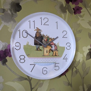 May include: White round clock with black numbers and a picture of rabbits in a classroom. The clock has a grey hour hand and a black minute hand.