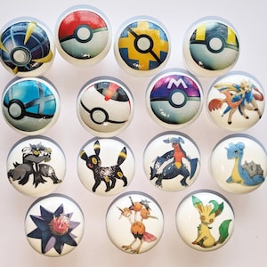 May include: Set of 15 round white ceramic drawer knobs with various Pokemon designs. The designs include Pokeballs, Pokemon characters, and a Pokeball with the letter M.